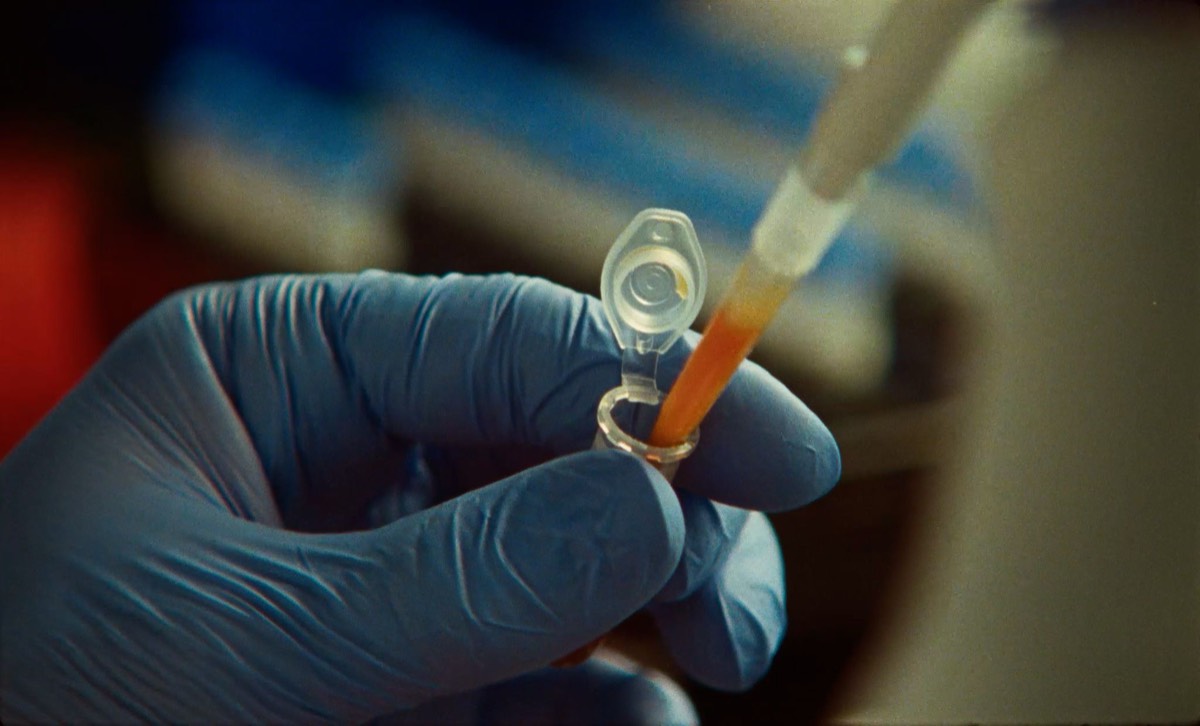 A gloved hand adds reagent to a microcentrifuge tube in a lab