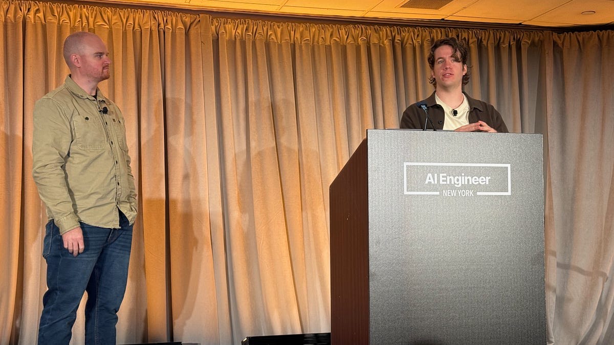 Speakers on stage at AI Engineer New York, one behind the event podium and one by the curtain