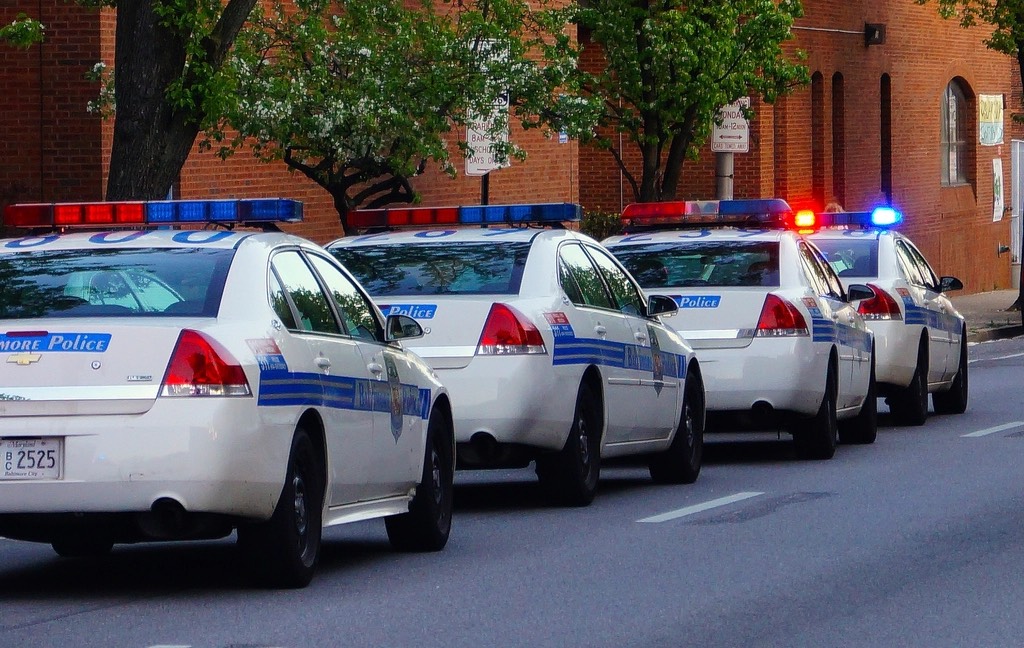 A row of Baltimore police cruisers parked at the curb, red and blue lights on