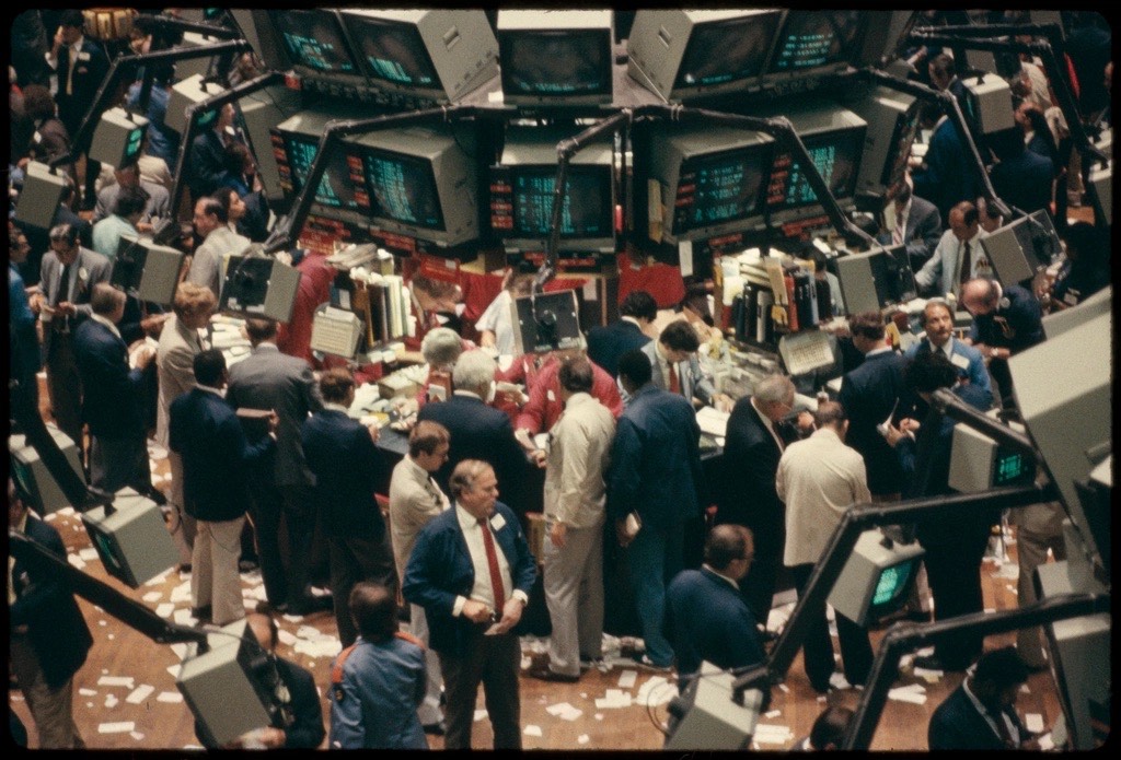 Historic photo of the New York Stock Exchange floor, traders gathered under quote screens