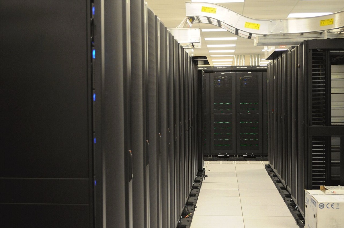A data hall aisle lined with black server cabinets, green status lights glowing on the racks at the far end