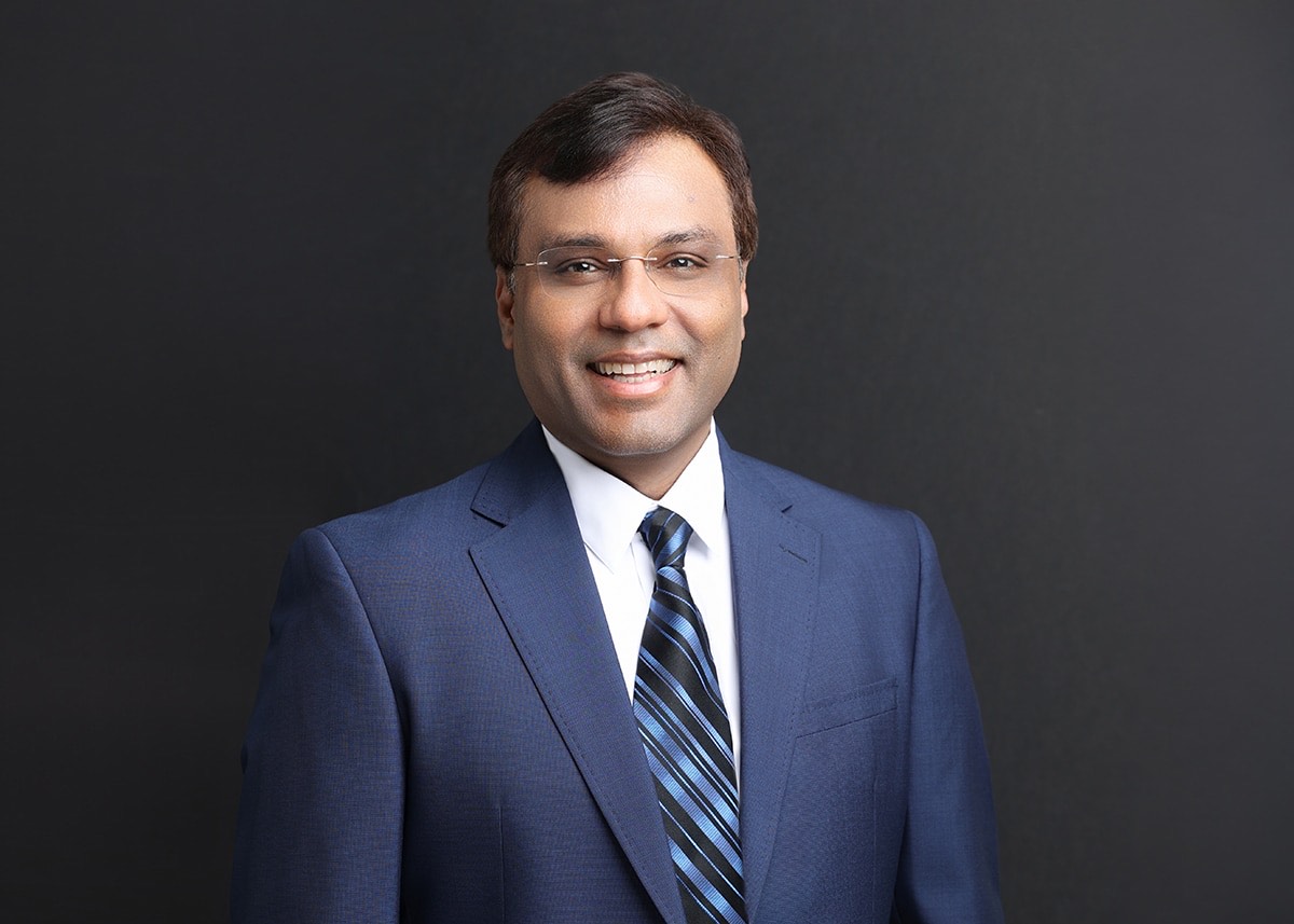 Official portrait of new Boston Dynamics CEO Rohit Prasad in a navy suit against a dark background