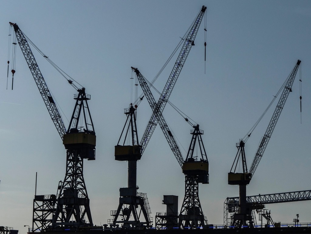 Silhouettes of four gantry cranes at a port against an empty dusk sky