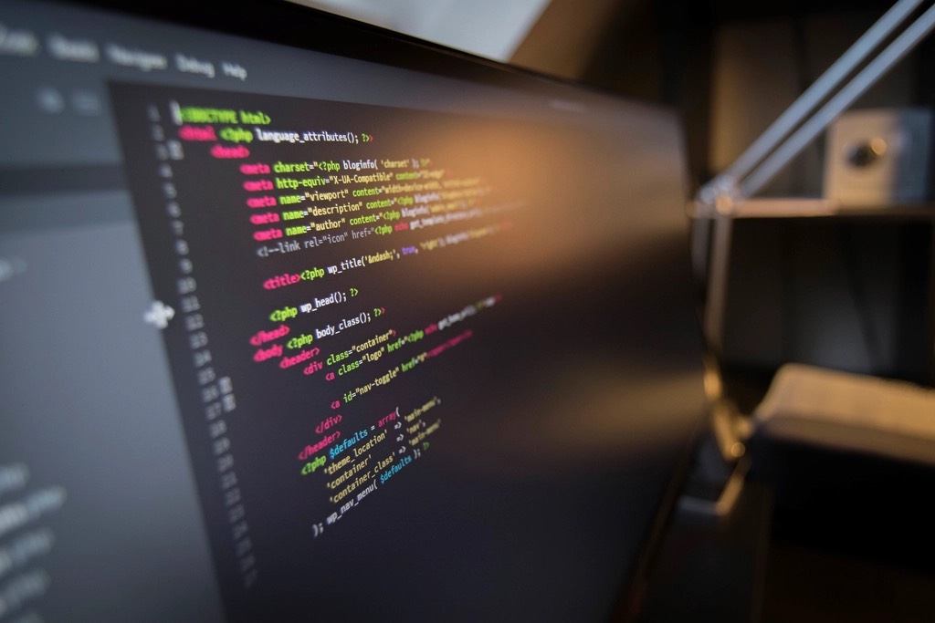 Colorful syntax-highlighted web template code on a dark monitor, a desk lamp glowing in the background
