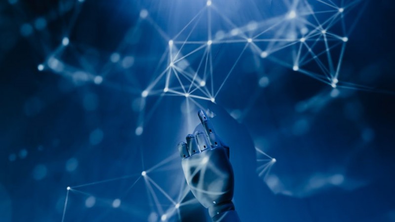 A metallic robotic hand points toward a glowing network of nodes and lines on a blue background