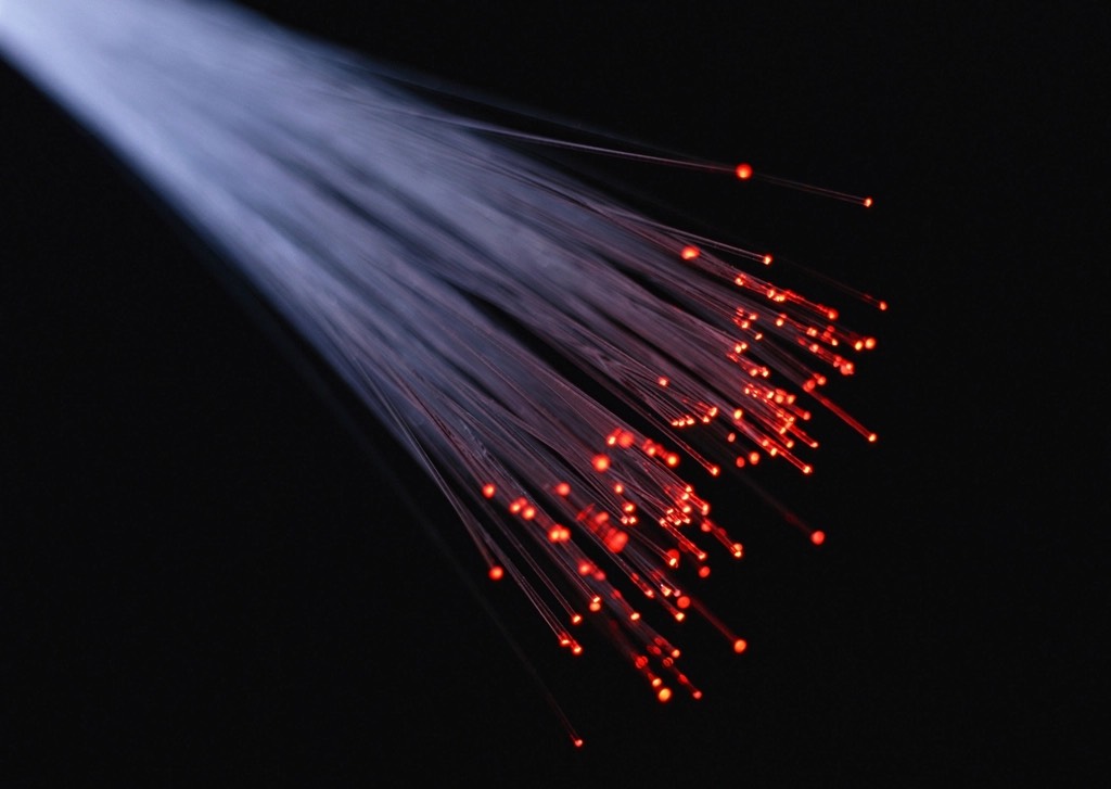 A bundle of optical fibers fanning out against a dark background, with red light glowing at their tips
