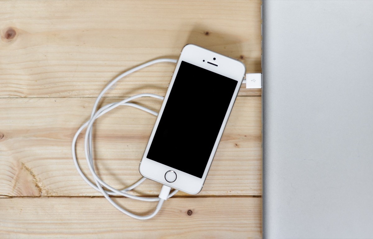 木桌上连着充电线的白色 iPhone 与笔记本电脑