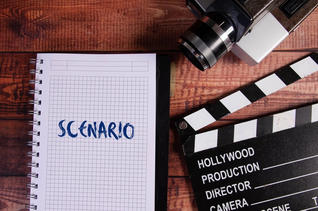 A spiral-bound shot-grid notebook, a clapperboard and a vintage camera on a wooden table, seen from above
