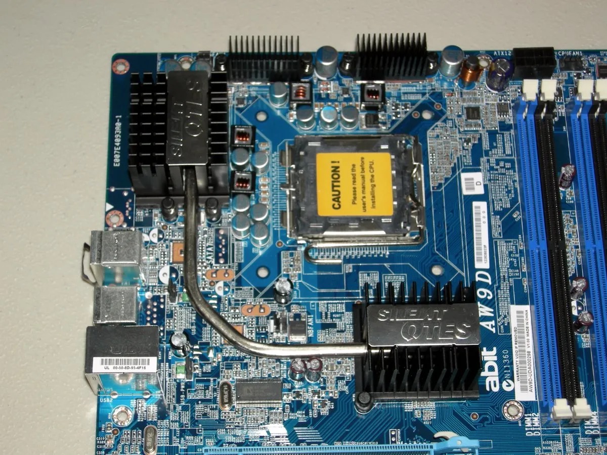 Close-up of an Abit AW9D motherboard, with a yellow CAUTION label on the CPU socket and heatsinks and capacitors around it