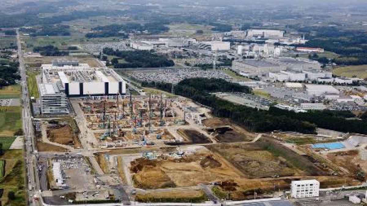 航拍视角下的熊本厂区:前景是塔吊与正在施工的场地,后方和右侧是已建成的白色厂房,四周是农田