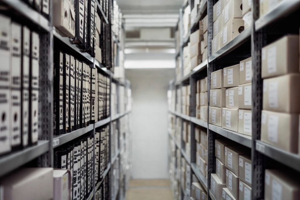 A narrow aisle between metal shelves stacked with archive boxes and binders