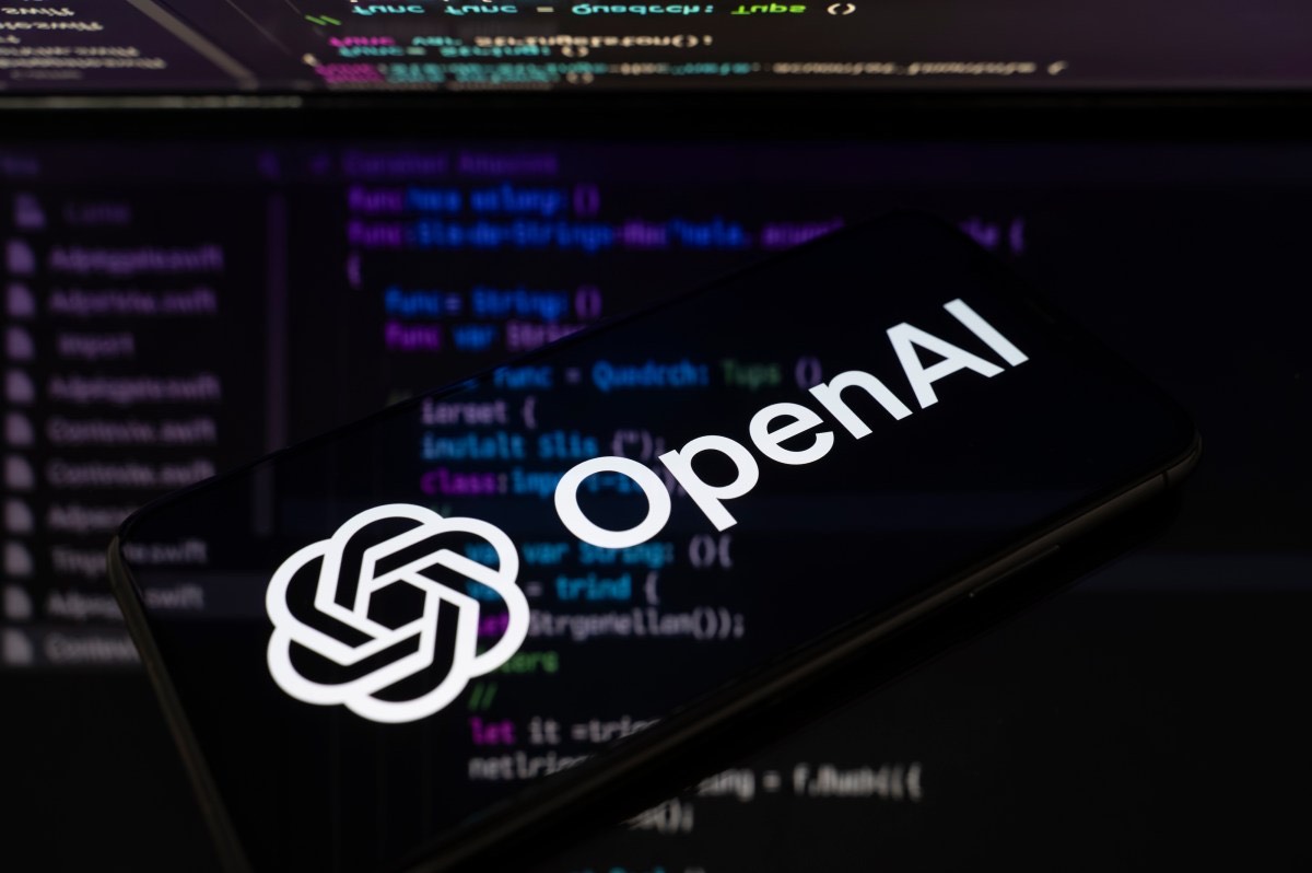 A phone showing the OpenAI logo in front of code on a screen