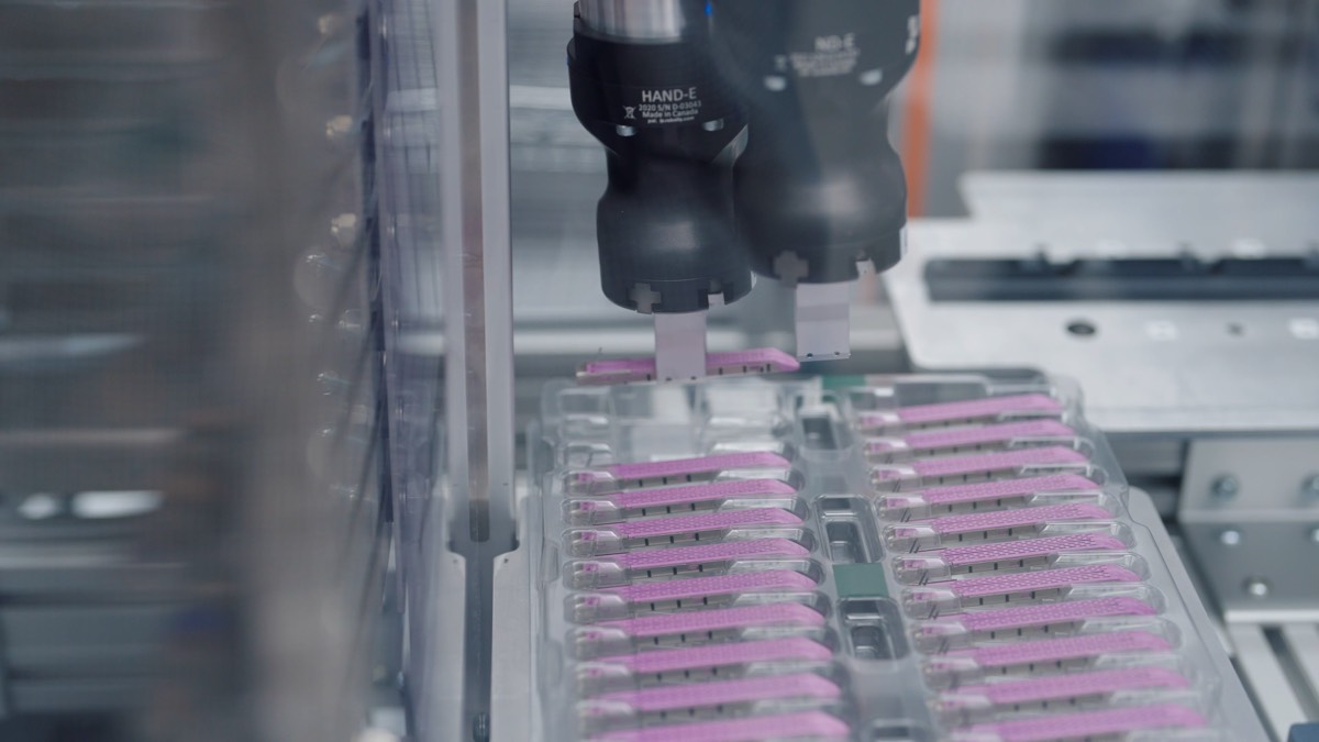 A robot gripper placing pink parts into trays on an assembly line