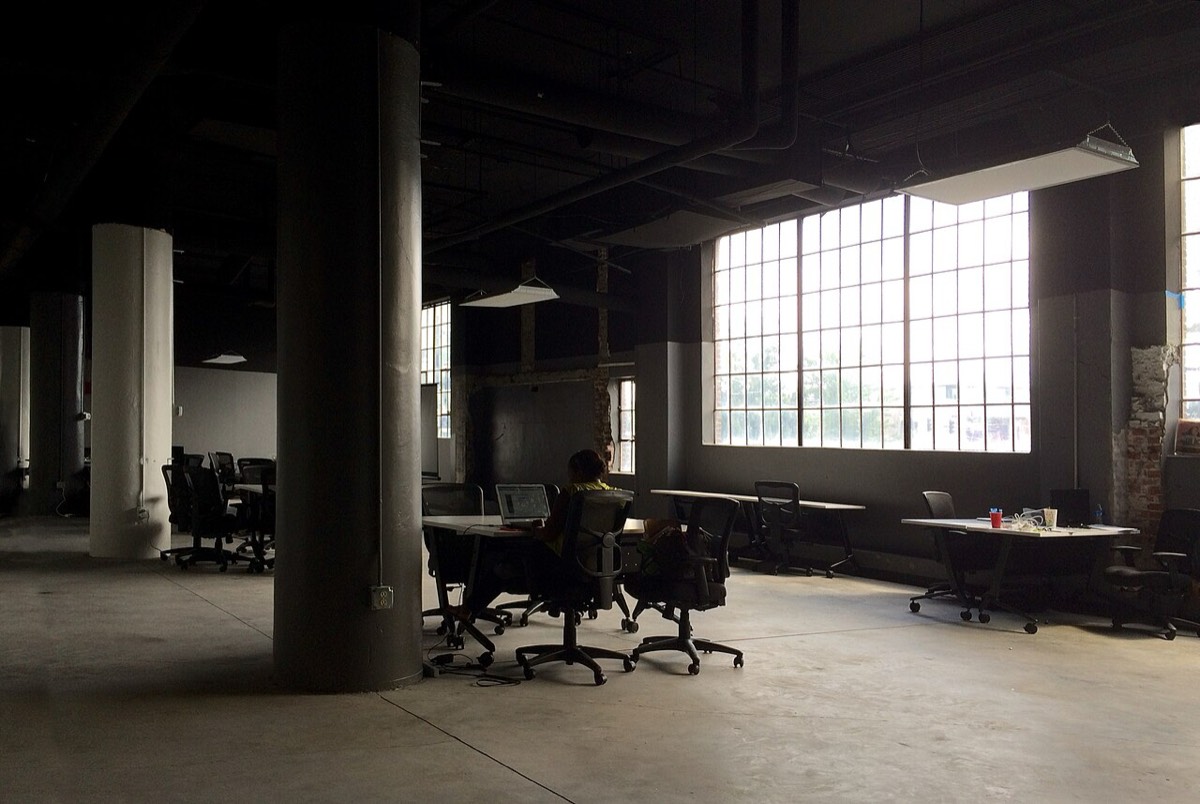 One person working alone on a laptop in a near-empty open-plan office lined with vacant chairs