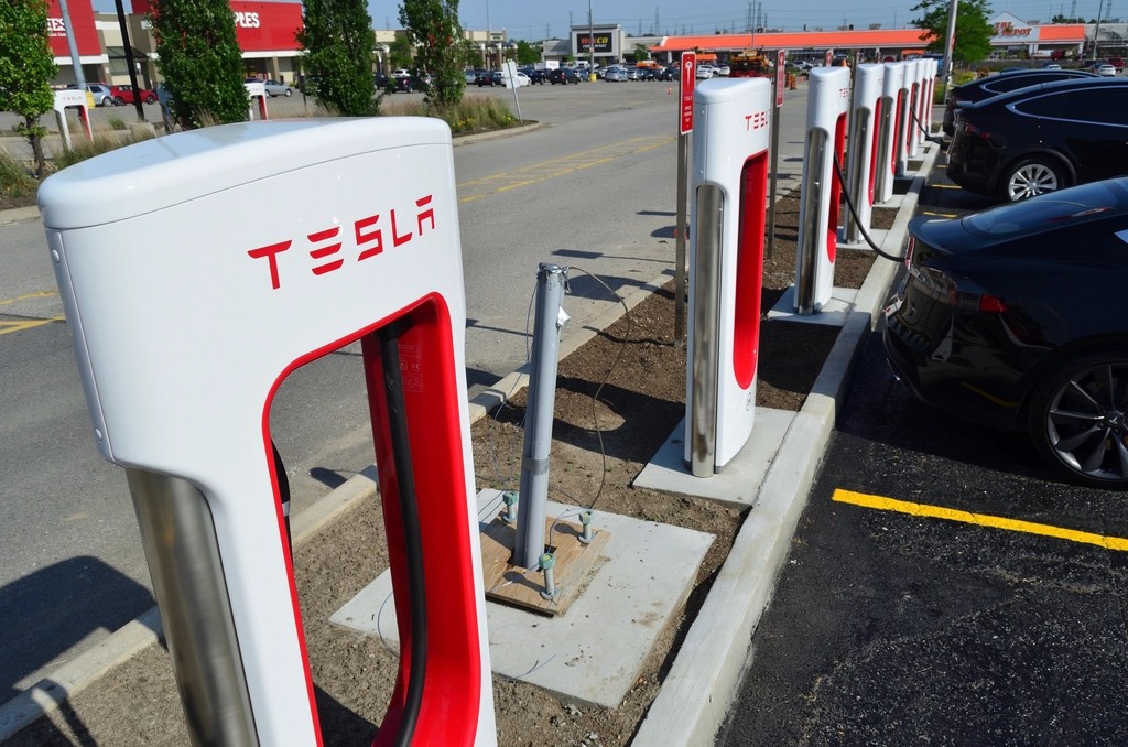 A row of red-and-white Tesla Supercharger stations at a retail parking lot