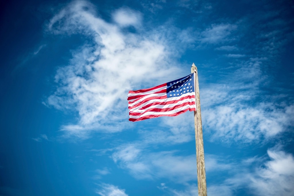 A US flag against a blue sky with clouds